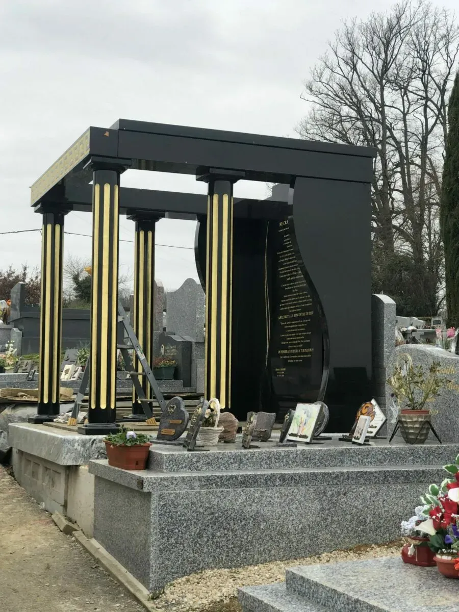 Grand monument funéraire en granite noir à colonnes dorées dans un cimetière.